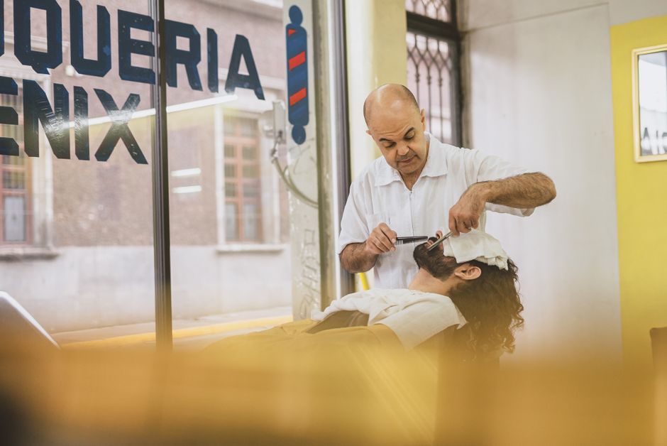 Barber performing a classic straight razor shave on a client in a bright barbershop.