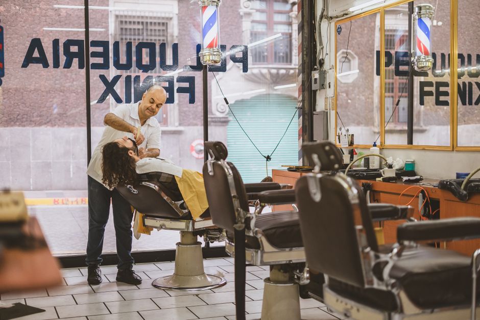 A barber expertly shaves a client's face in a classic barbershop setting.